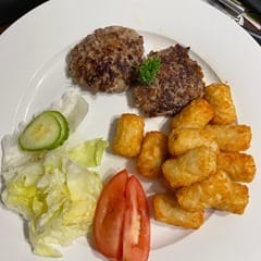 A white plate containing 2 beef rissoles, potato gems, tomato, lettuce & cucumber.